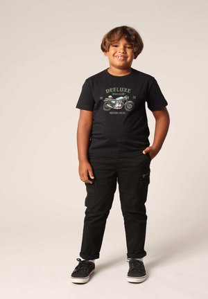 Zwart T-shirt met korte mouwen met een motorgraphics en groene tekst, vernoemd met zwarte cargobroeken en zwarte sneakers.