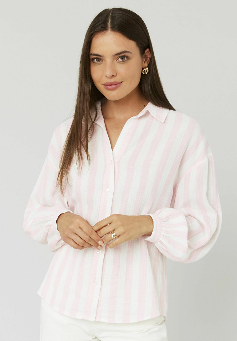 Chemise à boutons rayée rose clair et blanche avec col, manches longues et poignets froncés. Texture douce et coupe décontractée.