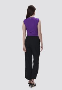 Top viola senza maniche abbinato a pantaloni neri a vita alta; il tessuto appare liscio. Scarpe nere con tacco completano l'outfit.