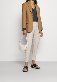 Brun överdimensionerad kavaj, marinblå v-ringad topp, beige byxor, svarta platåsandaler, vit axelväska. Släta texturer, neutral färgpalett.