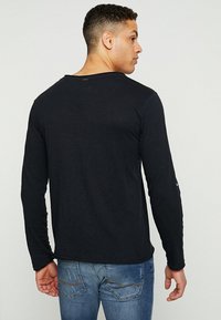 Camiseta negra de manga larga con cuello redondo, textura suave y sutiles detalles de costura, combinada con jeans de mezclilla azules.