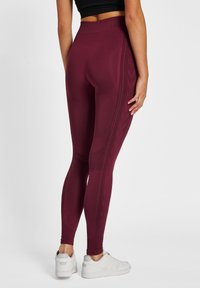 Leggings burdeos con una cintura alta, con patrones texturizados a lo largo de los lados, hechos de un material elástico. Combinados con zapatillas blancas.