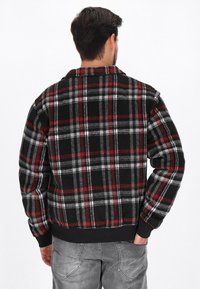 Schwarz-rote-graue karierte Flanelljacke mit Kragen, langen Ärmeln und gerippten Bündchen. Der Stoff wirkt weich.