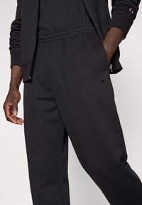 Μαύροι φόρμες με ελαστική μέση και πλαϊνές τσέπες. Κατασκευασμένοι από μαλακό ύφασμα, με μικρό λογότυπο στο αριστερό μπροστινό μέρος του μηρού.