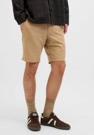 Pantalones cortos de algodón beige con un ajuste regular, que presentan bolsillos laterales y un dobladillo recto. Combinados con zapatillas de ante marrón y calcetines beige.