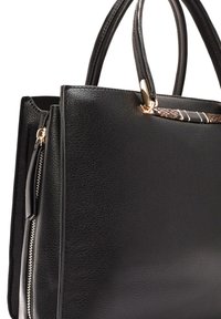 Sac fourre-tout en simili cuir noir avec deux poignées, extérieur texturé, poche zippée et accent avec motif sur le bord supérieur. Détails en matériel doré.