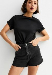 Camiseta de algodón negra con mangas enrolladas, combinada con shorts de mezclilla negros de talle alto con dobladillos desgastados y bolsillos frontales.