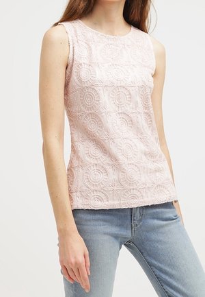 Haut sans manches rose clair avec des motifs en dentelle circulaires porté avec un jean bleu clair, visible du cou aux hanches.