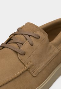 Gros plan d'une chaussure décontractée en daim beige avec des lacets marron assortis et une couture détaillée sur une semelle beige.