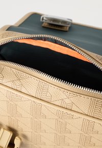 Μπεζ δερμάτινη τσάντα με ανάγλυφο μοτίβο, μερικώς ανοιχτό ασημένιο φερμουάρ, που αποκαλύπτει εσωτερικό από μαύρο και πορτοκαλί ύφασμα.