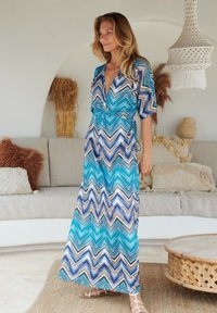 Maxi-Kleid mit einem Zickzackmuster in Blau, Weiß und Braun. Aus leichtem Stoff mit einem tiefen Ausschnitt und verstellbarem Taillenbund.