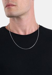 Söljdkedja, med länkar som har en slät yta, bärs över en svart T-shirt med rund halsringning, vilande strax under nyckelbenet.