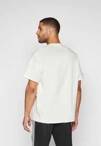 Tričko s krátkym rukávom a okrúhlym výstrihom v off-white farbe. Má voľný strih, hladkú textúru a jednoduchý dizajn bez viditeľného loga alebo vzorov.