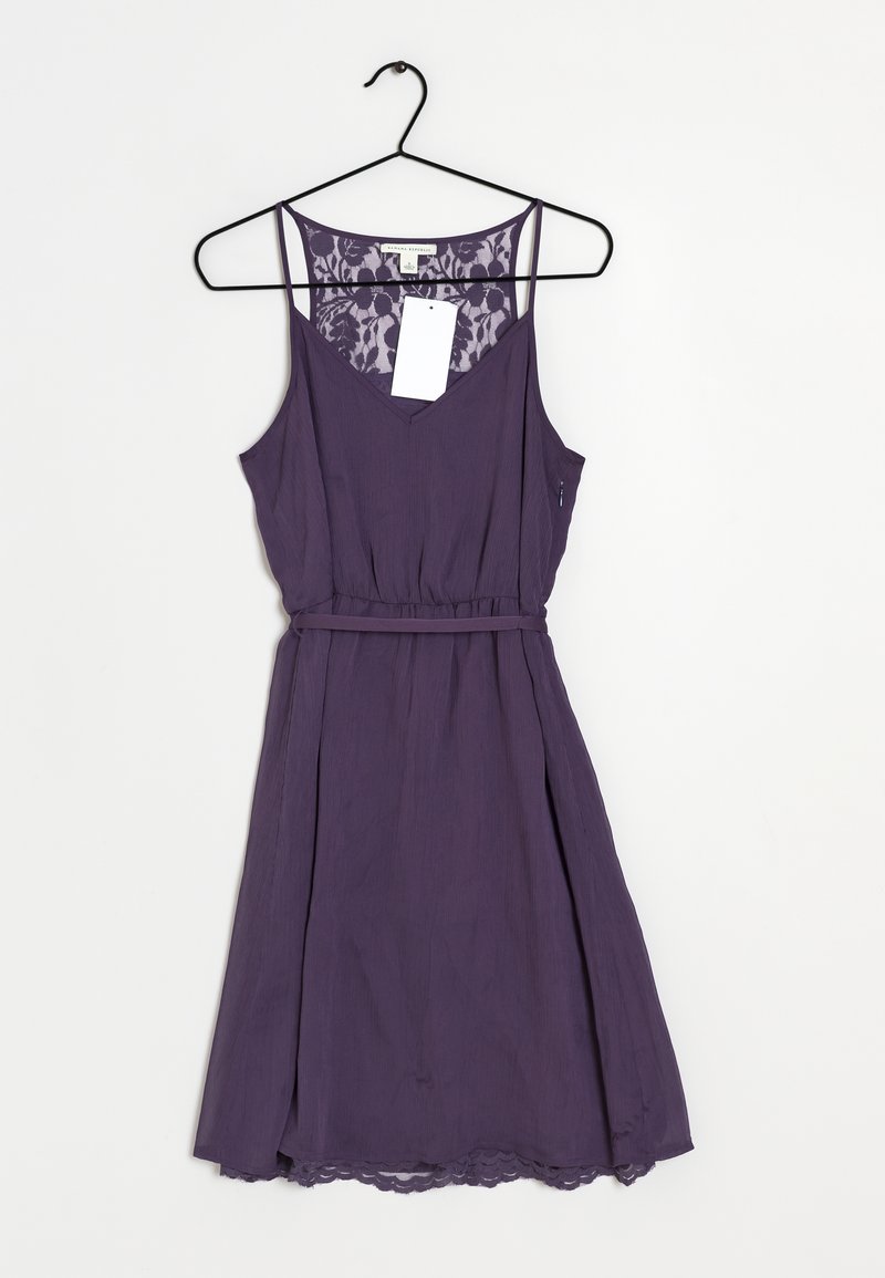 Lilla ærmeløs kjole med v-hals, bæltestrop om taljen, tekstureret stof, blonderdetalje på ryggen og bølget kant.