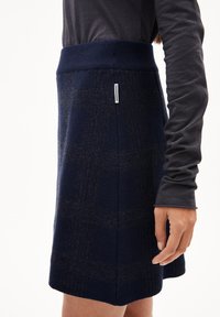 Marineblaue Wollröcke mit einem strukturierten Karomuster, ausgestattet mit einem gestrickten Bund und seitlichem Etikett. Der Saum ist gerade und leicht ausgestellt.