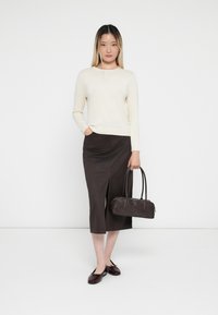 Beige sweater, dark brown midi skirt with slit, black handbag, and burgundy shoes. Smooth textures, casual design, neutral color palette.