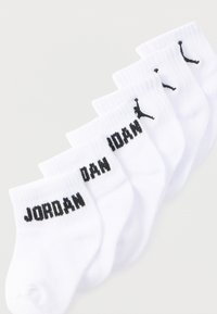 Πέντε ζευγάρια λευκές κάλτσες αστραγάλου με μαύρο κείμενο "JORDAN" και το λογότυπο Jumpman τοποθετημένα διαγώνια πάνω σε λευκό φόντο.