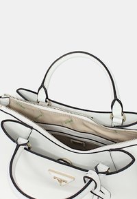 Borsa bianca con finitura testurizzata, dettagli neri, doppio manico e zip. L'interno presenta un rivestimento beige con un motivo a logo verde.