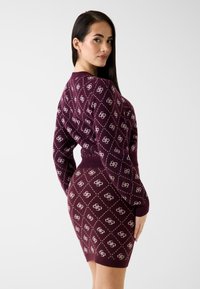 Rochie tricotată bordo cu un model în formă de diamant și accente crem, având mâneci lungi și o siluetă ajustată. Textură netedă.