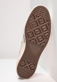 Podeszwa trampec Converse All Star, wykonana z brązowego materiału gumowego z teksturowanym geometrycznym wzorem i logo. Klasyczne białe boki.