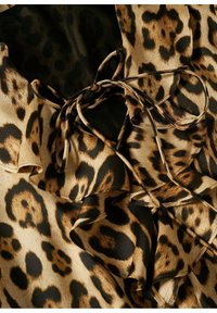 Tkanina w lamparcie cętki w odcieniach brązu, beżu i czerni. Posiada falbany na brzegach oraz wiązanie, co nadaje teksturowany wygląd.