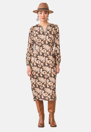 Mujer con vestido midi marrón con estampado floral y mangas largas, sombrero ancho color tostado, grandes pendientes en forma de gota y botas marrones hasta la rodilla.