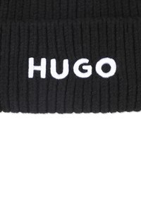 Cappello beanie a coste nere con il logo ricamato bianco "HUGO" in evidenza sul davanti. Realizzato in tessuto morbido e testurizzato.