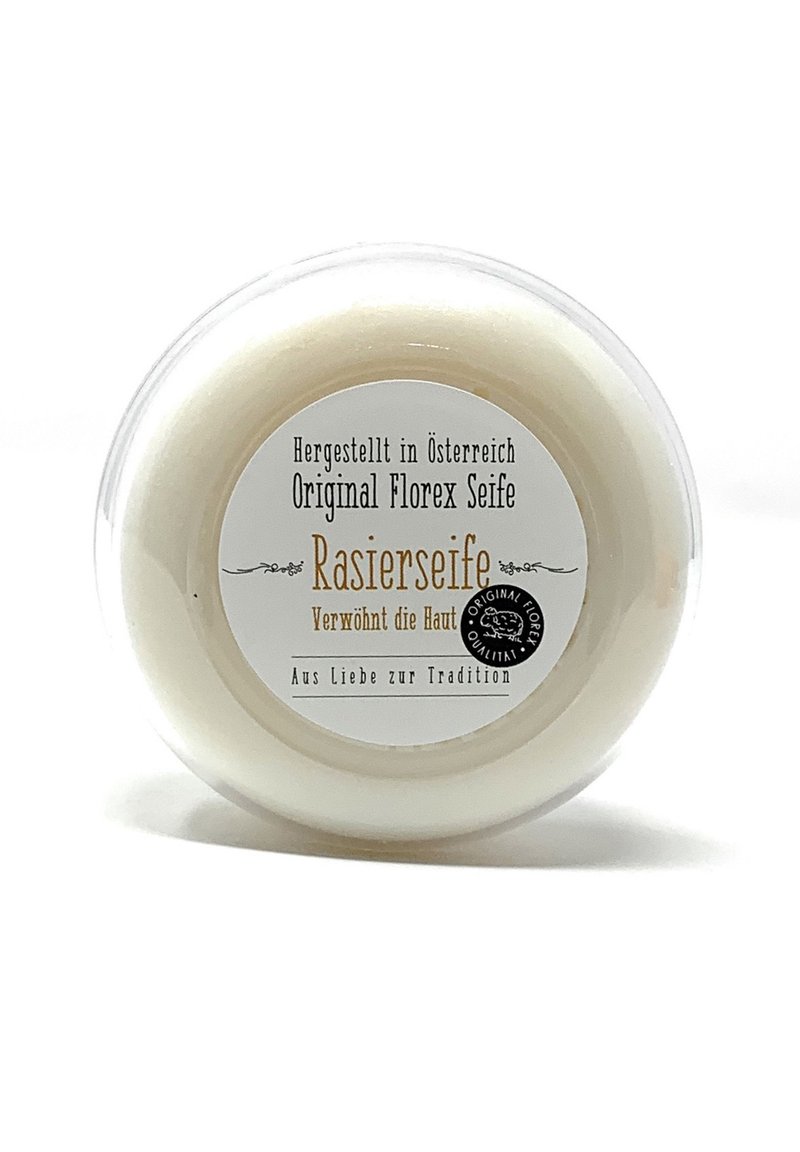 White, circular shaving soap in a clear, plastic container. Label features black and gold text, detailing origin and product name. Smooth texture.
