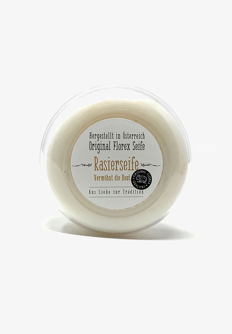White, circular shaving soap in a clear, plastic container. Label features black and gold text, detailing origin and product name. Smooth texture.