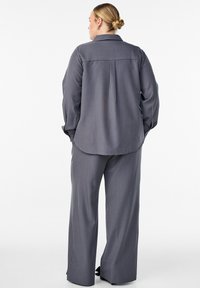 Sivý tkaný úbor so voľným strihom, ktorý pozostáva z košele na gombíky s golierom a širokých nohavíc, oboje s jemnou textúrou a minimálnymi švami.