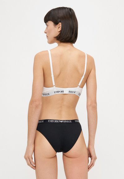 Bralet alb cu bretele ajustabile și bandă elastică etichetată "EMPORIO ARMANI", asociat cu chiloți negri cu un tiv similar ce poartă logo-ul.