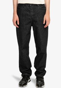 Jeans de mezclilla negra con un ajuste relajado, que presentan un diseño de cinco bolsillos, un ligero desvanecimiento y costuras en contraste. Combinados con zapatillas negras.