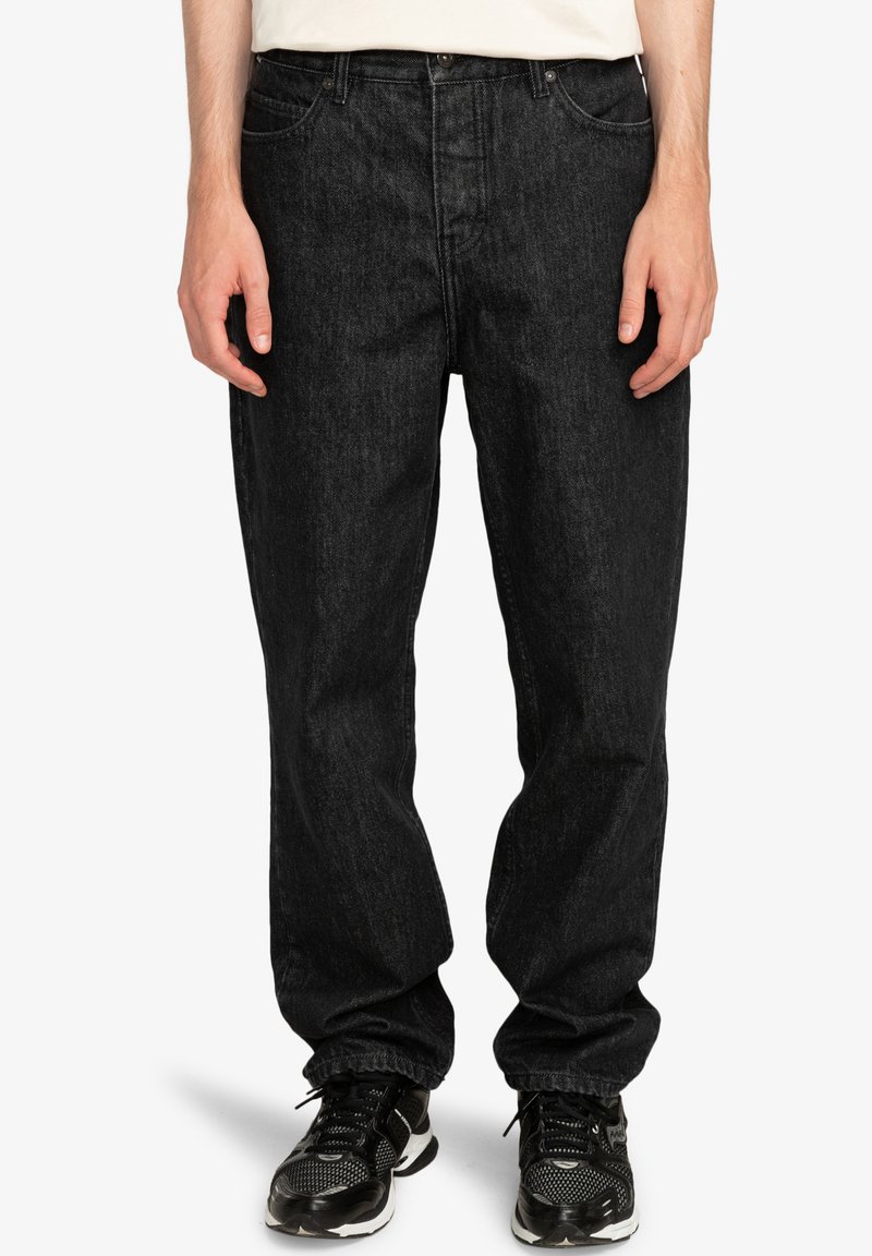 Jeans de mezclilla negra con un ajuste relajado, que presentan un diseño de cinco bolsillos, un ligero desvanecimiento y costuras en contraste. Combinados con zapatillas negras.