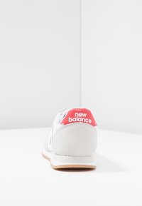 Baskets en daim gris avec des accents blancs, dotées d'une languette rouge au talon affichant le logo "new balance". Forme arrondie avec une finition texturée.