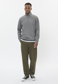 Lichtgrijze zip-nektroy, van een katoenmix, met een soepele textuur. Gecombineerd met lichtgroene broek met een relaxed fit en zwarte lage sneakers.