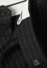 Czarna tkanina w prążki z białymi akcentami, z przezroczystym guzikiem i usztywnionym kołnierzykiem. Zawiera widoczne detale szycia.