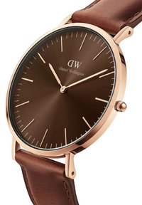 Brown dial watch with gold-tone case and brown leather strap. Markers are thin and elongated. Features a crown for time adjustment.