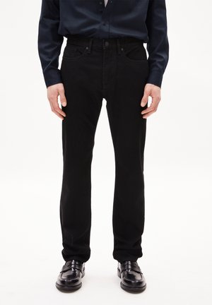 Black denim jeans with a straight fit, featuring five pockets, a zip fly, and contrasting stitching details. Worn with black shoes.