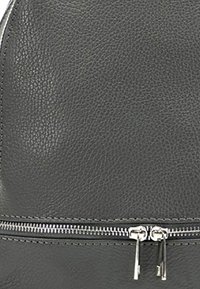 Sac à dos en cuir gris avec une surface texturée et une fermeture éclair argentée en bas. Bords lisses avec des détails matériels minimaux.