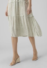 Vihreä, kuvioitu midi-mekko, jossa on röyhelökerroksia. Yhdistettyinä läpinäkyviin, korkokenkiin, joissa on neliön muotoinen kärki.