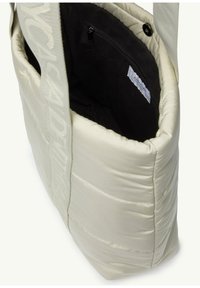 Padded cream tote bag with a textured finish, featuring a black interior pocket and a wide, logo-embossed strap.