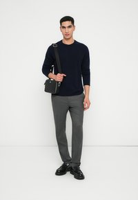 Maglione a maglia marina, pantaloni grigi su misura, borsa a tracolla nera con hardware argentato e scarpe nere chunky. In piedi su uno sfondo bianco.