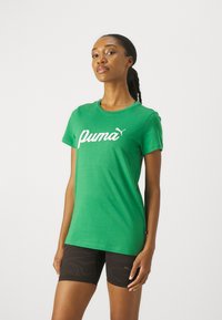 Zielona koszulka bawełniana z białym logo "Puma". Okrągły dekolt i krótkie rękawy. W zestawie z czarnymi spodniami w wzory.