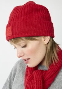 Rote Strickmütze mit strukturiertem Rippdesign, kombiniert mit einem passenden roten Schal. Der Schal ist in einem ähnlichen Rippmuster gestrickt.