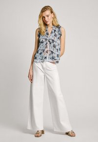 Ziedu raksta bezpiedurkņu blūze zilā un baltā krāsā ar frēzētu apkakli, kombinēta ar platajām baltajām biksēm un zelta siksniņu sandālēm.