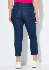 Tmavě modré denimové capri kalhoty se strečovým pasem, vybavené dvěma zadními kapsami a úzkým střihem, doplněné bílými teniskami.