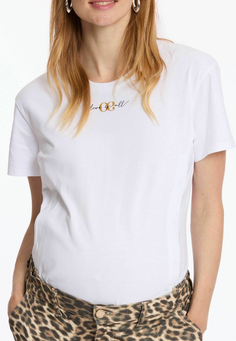 T-shirt en coton blanc à manches courtes, avec un design en écriture dorée "love & all" sur la poitrine. Associé à un pantalon à imprimé léopard.