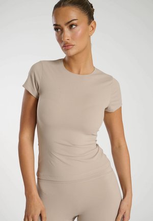 Haut ajusté beige à manches courtes en matériau doux et extensible, avec un col rond et une texture lisse, présentant un léger ruché sur les côtés.