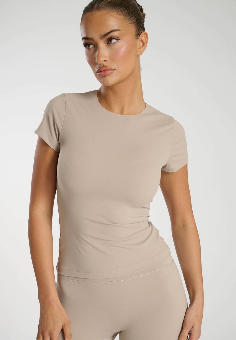 Beige, figurnära t-shirt med kort ärm som är gjord av mjukt, elastiskt material. Den har en rund halsringning och en slät yta, samt diskret sidoveck.