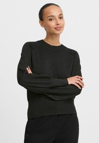 Schwarzer Strickpullover mit rundem Halsausschnitt, Raglanärmeln und entspannter Passform. Verfügt über einen subtilen Glanz sowie gerippte Bündchen und Saum.